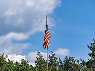 US flag on flagpole against blue sky and trees in background